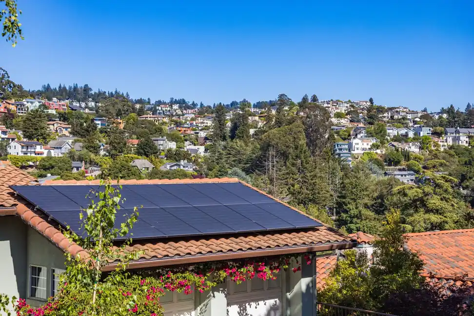 Paneles solares sobre un tejado de teja roja de una vivienda con buganvillas en flor
