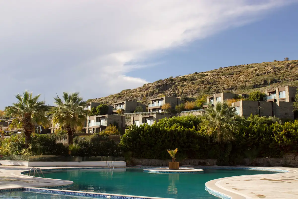 Piscina de un complejo de apartamentos con palmeras y casas de piedra en la ladera