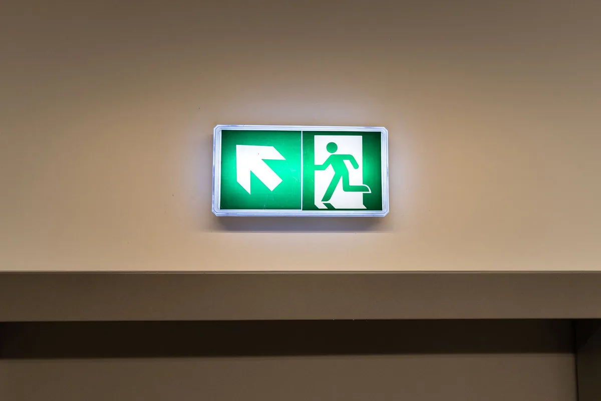 Señal luminosa de salida de emergencia con flecha y figura en la pared de un pasillo