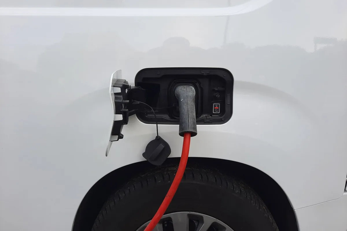 Cable rojo enchufado en la toma de carga de un coche eléctrico blanco, con la tapa abierta