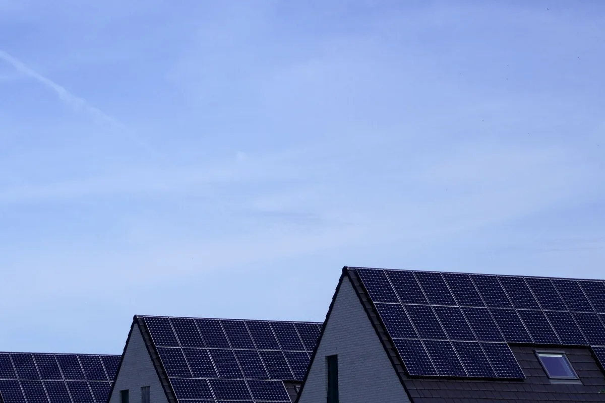Dos tejados a dos aguas cubiertos de placas solares bajo un cielo azul pálido