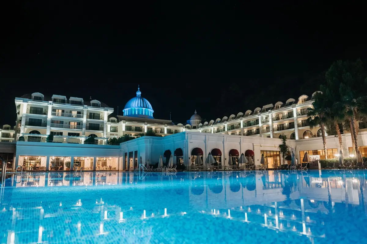 Hotel grande iluminado de noche junto a una piscina de agua azul