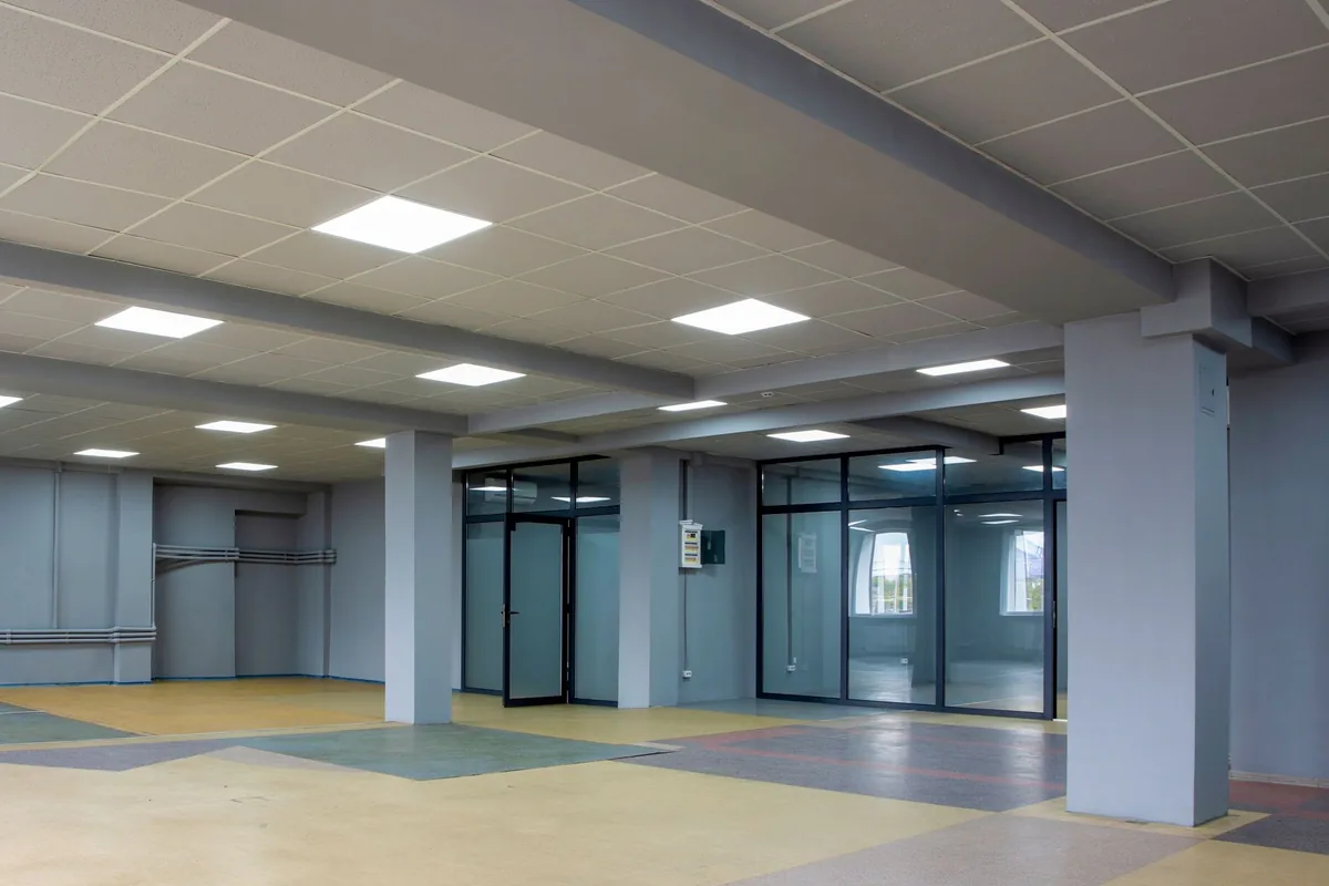 Local diáfano sin muebles, con paneles LED en el techo, pilares grises y mamparas de cristal al fondo