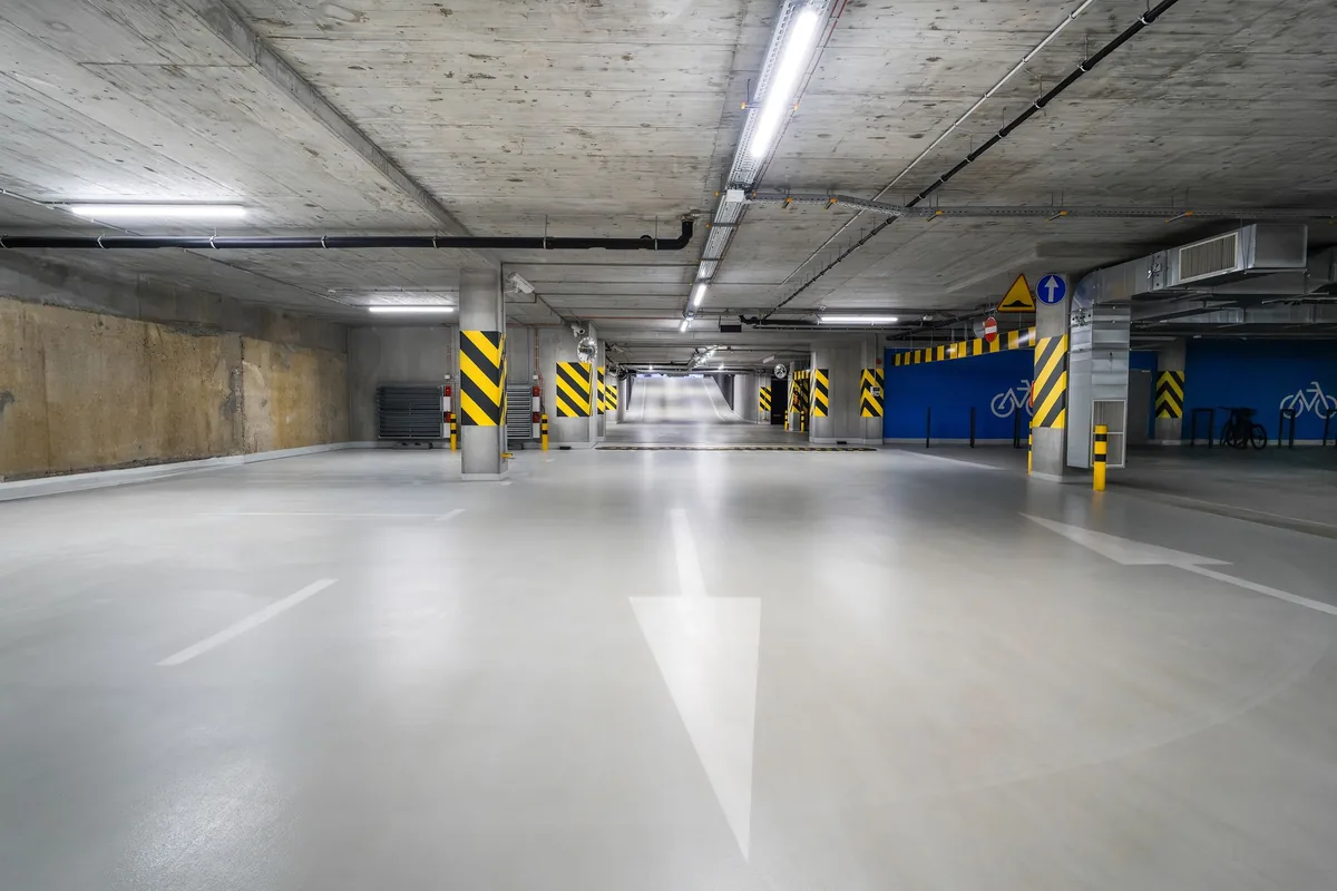 Garaje subterráneo vacío de un edificio, con suelo gris, flechas pintadas y columnas con franjas amarillas y negras
