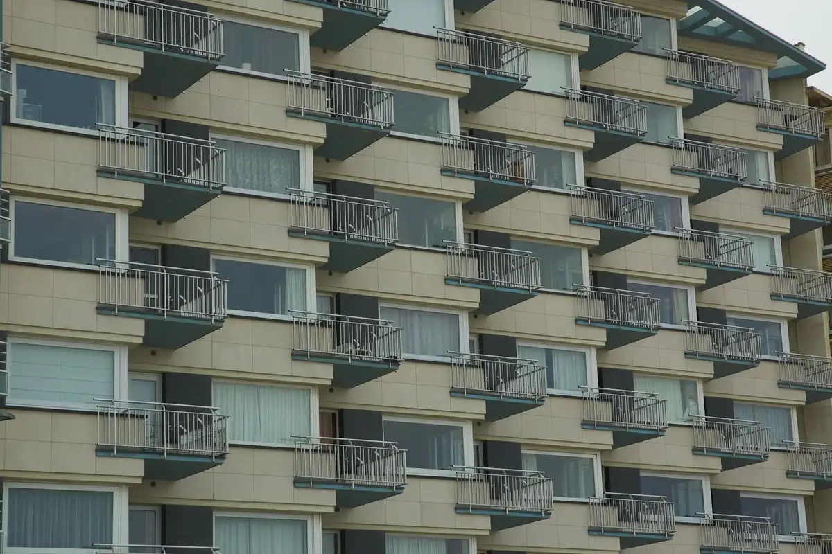 Fachada beige de un bloque de pisos con balcones de barandilla metálica y grandes ventanas