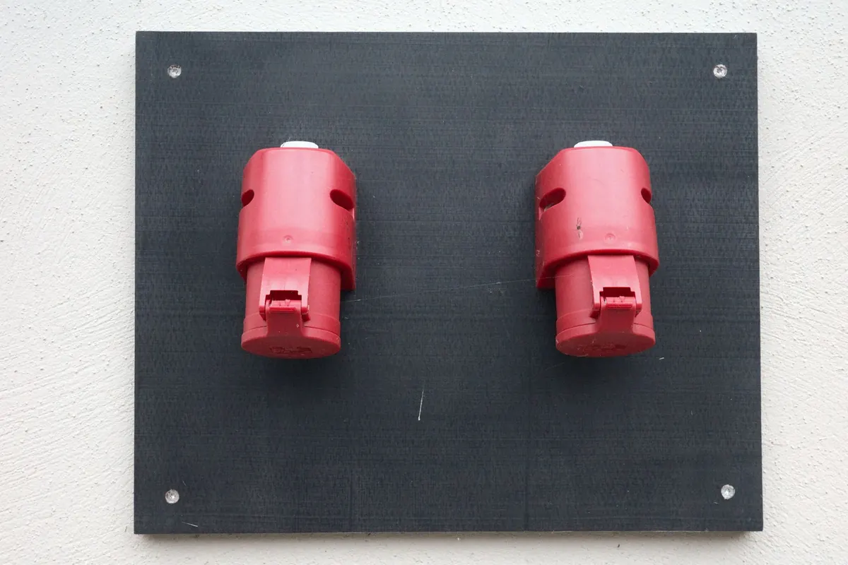 Dos tomas eléctricas industriales rojas montadas sobre una placa negra en un muro