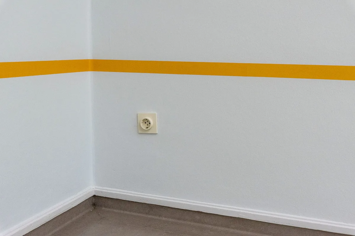 Enchufe de pared en la esquina de una habitación pintada, con una franja amarilla