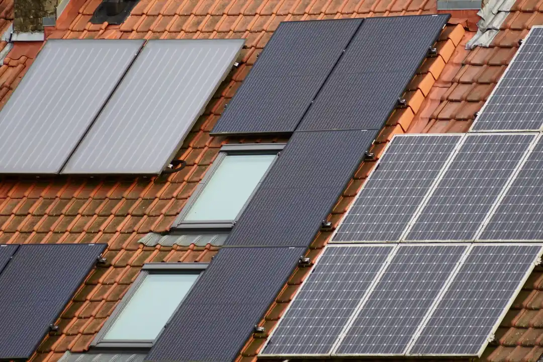 Placas solares oscuras y un panel térmico sobre un tejado de tejas rojas