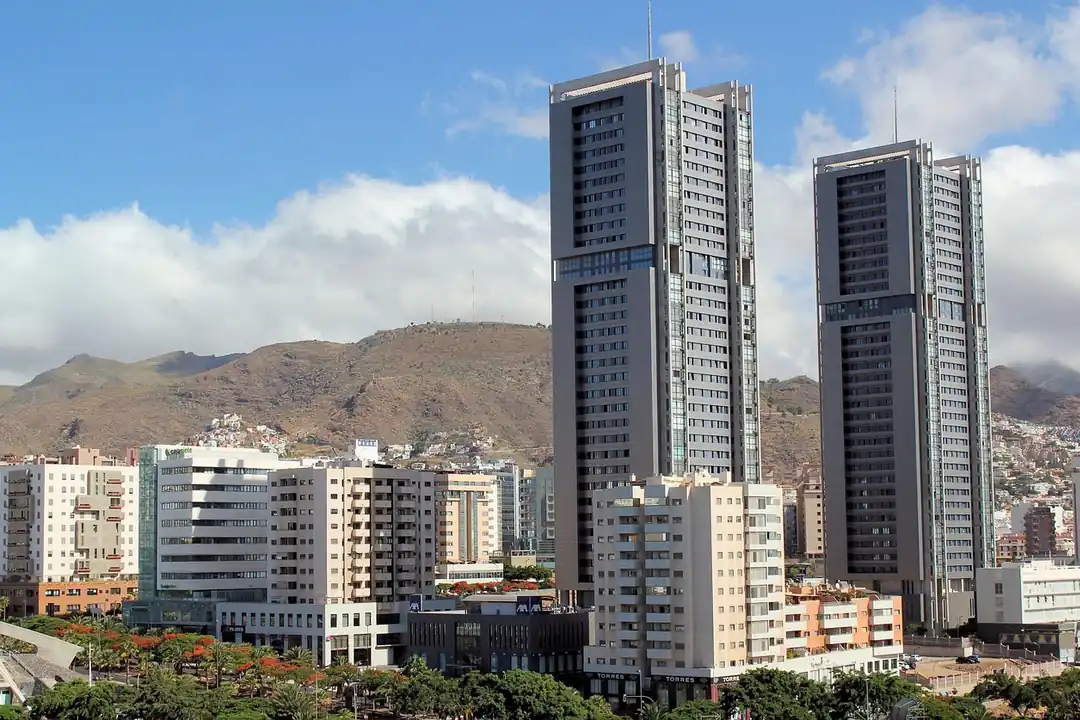 Torres y bloques de viviendas de una ciudad, con montañas secas al fondo y nubes sobre las cumbres