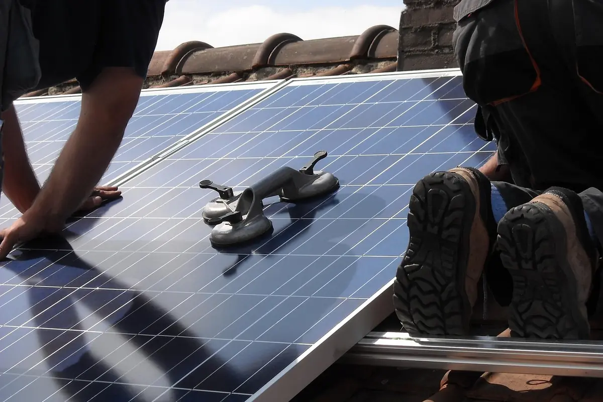 Dos operarios colocan un panel solar sobre una cubierta de teja, con una ventosa para moverlo