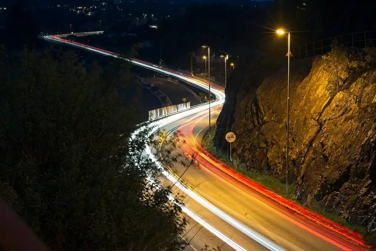 Carretera de curvas de noche con farolas encendidas y estelas de luz de los coches