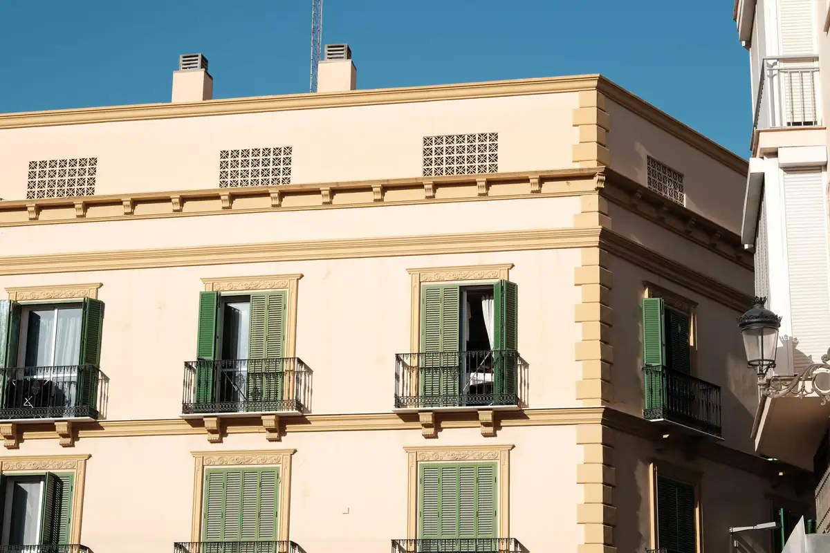 Edificio de viviendas de varias plantas con balcones de hierro y contraventanas verdes