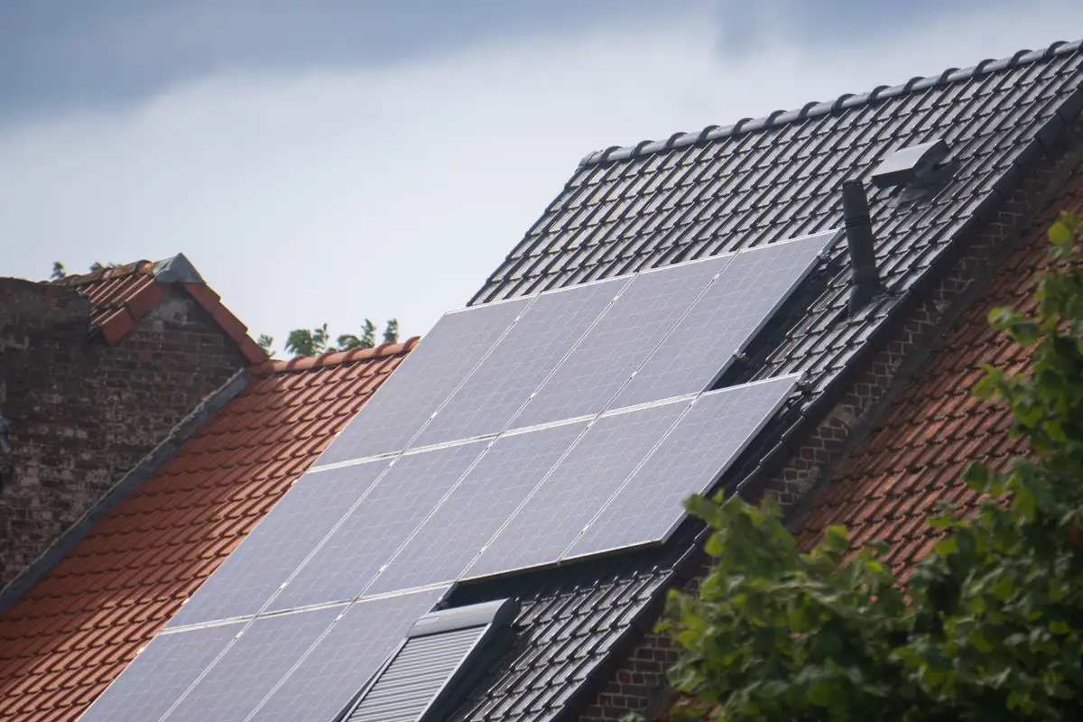 Placas solares instaladas en un tejado inclinado de tejas, con el cielo nublado detrás