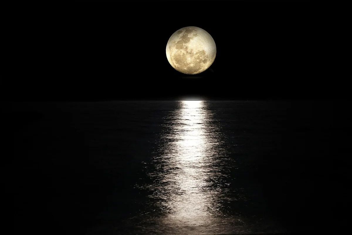 Luna llena sobre el mar en calma de noche, con su reflejo plateado en el agua