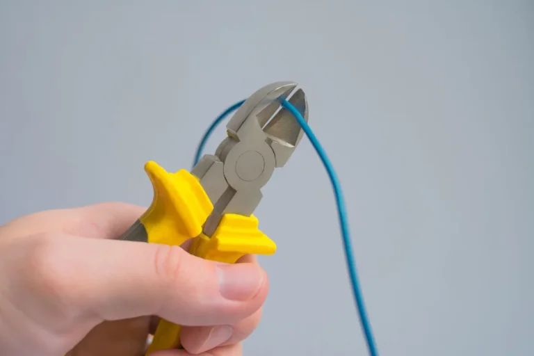 Mano de un electricista cortando un cable azul con unos alicates de corte